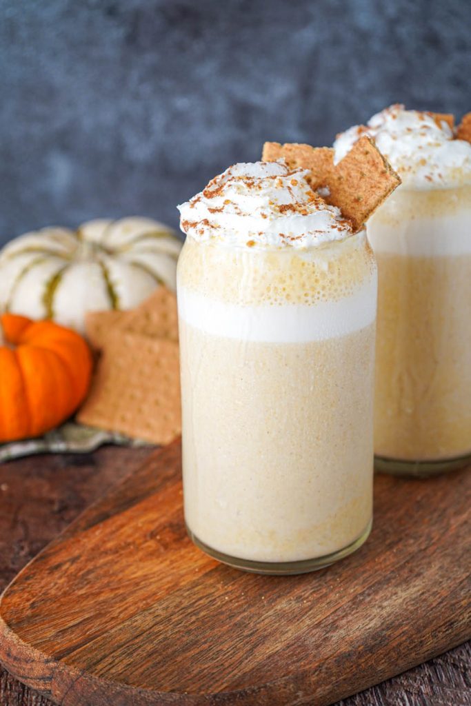 Side view of Pumpkin Cheesecake Smoothie in two glasses with pumpkins in the background.