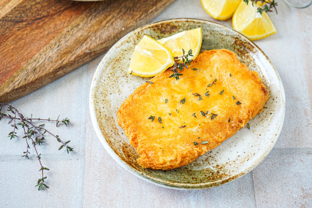 Saganaki (Greek Fried Cheese) on a plate with thyme leaves and two lemon wedges.