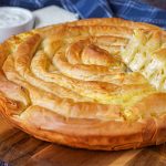 Banitsa (Bulgarian Cheese Pie) on a wooden board with a slice lifted up.