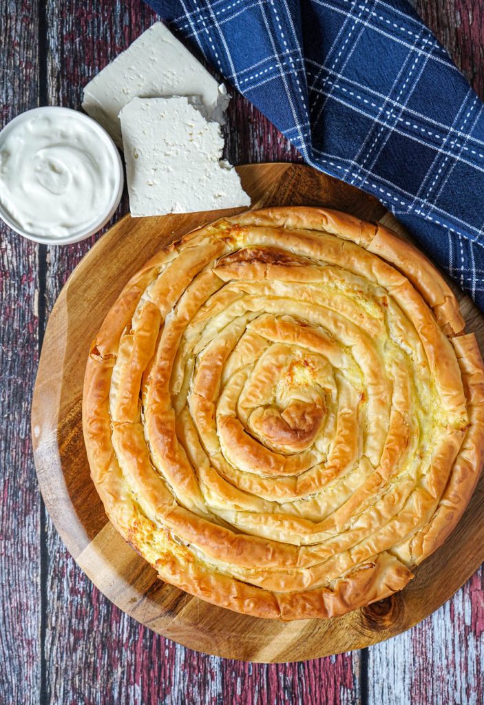Aerial view of Banitsa (Bulgarian Cheese Pie) on a wooden board next to yogurt and cheese.