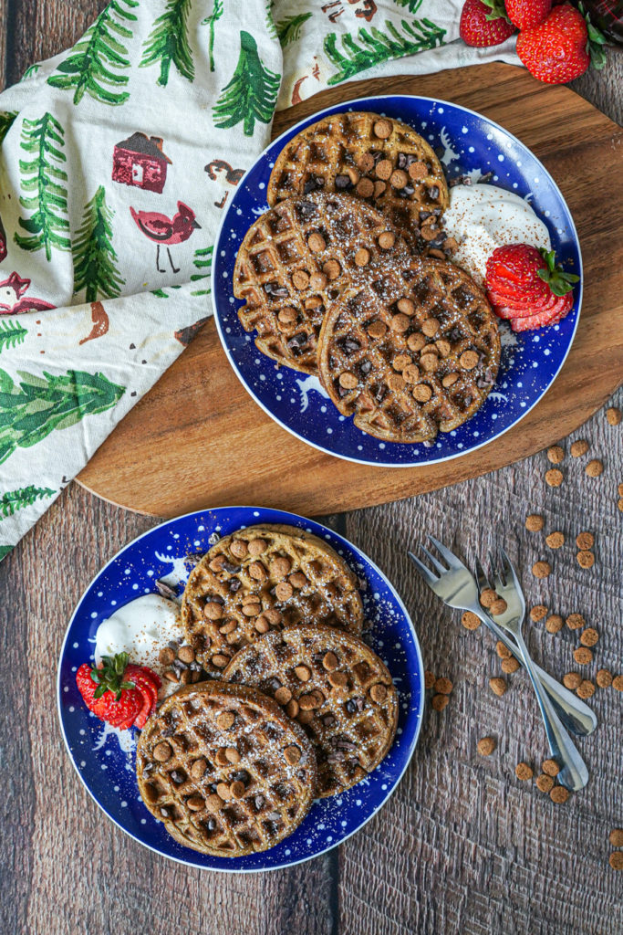 Aerial view of Gingerbread Waffles on two blue and white plates with whipped cream and strawberries.