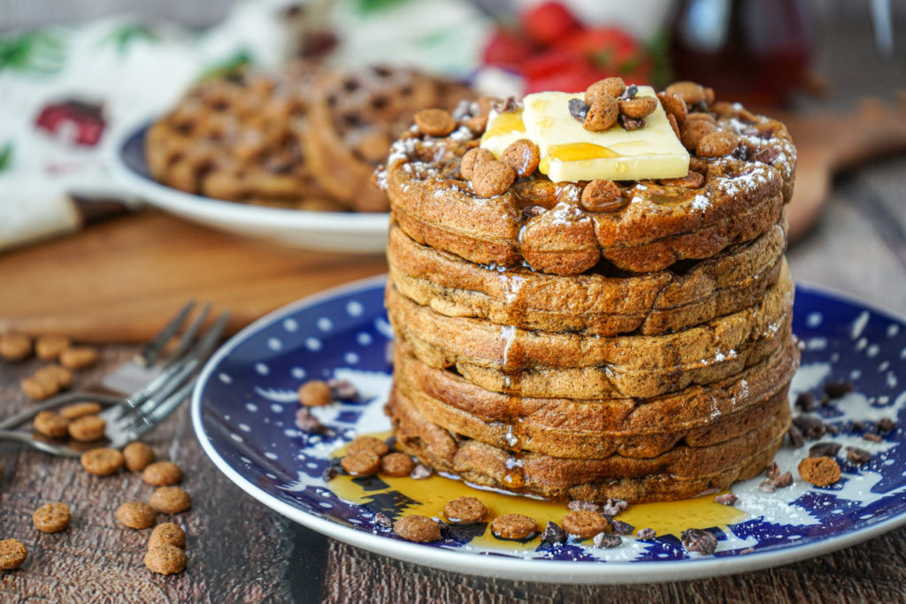 A stack of five Gingerbread Waffles on a blue plate and covered with butter, maple syrup, cacao nibs, and Schuddebuikjes.
