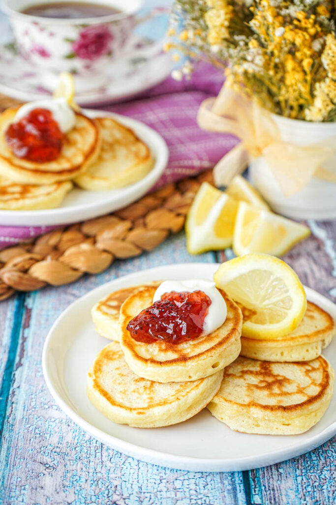 Lemon Pikelets on two white plates with flowers and a cup of tea in the background.