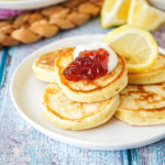 Lemon Pikelets on a white plate with strawberry jam, whipped cream, and lemon slices.