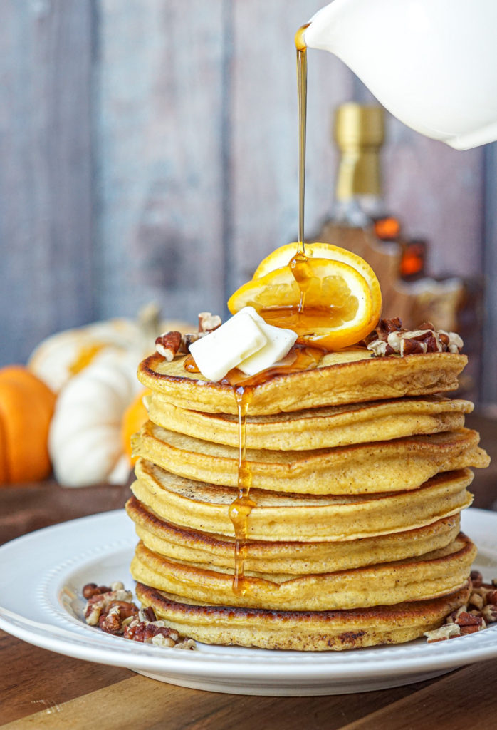 Drizzling maple syrup over a stack of seven Orange Pumpkin Pancakes.