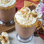 S'mores Milkshake in two glasses next to purple flowers, toasted marshmallows, and chocolate chips.