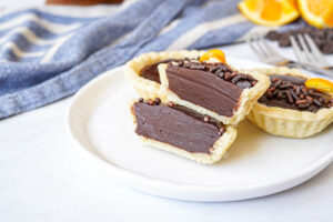 Three Chocolate Orange Ganache Tartlets on a white plate with one cut in half.