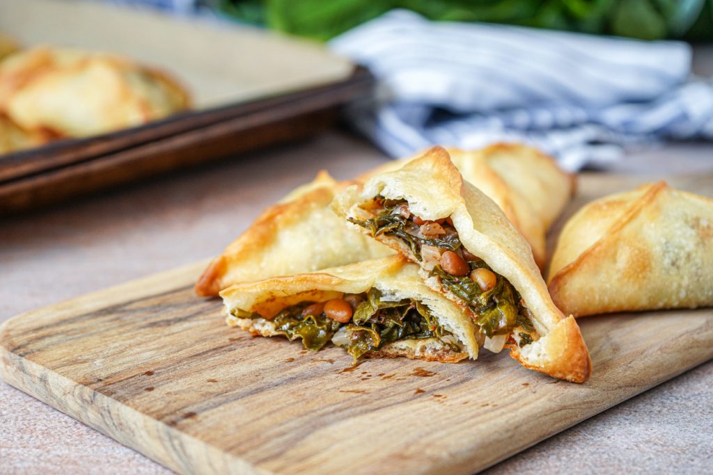 Fatayer bi Sabanekh (Lebanese Spinach Pies) on a wooden board with one cut in half.