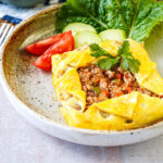 Kai Yad Sai (Thai Stuffed Omelette) in a bowl with lettuce, cucumber slices, and tomato wedges.