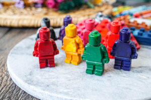Lego crayons shaped like people and bricks on a marble board.