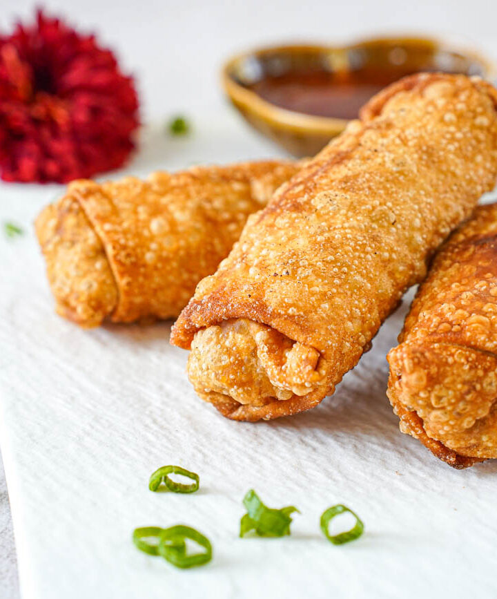 Three Pork Egg Rolls on a white plate with thinly sliced green onions.