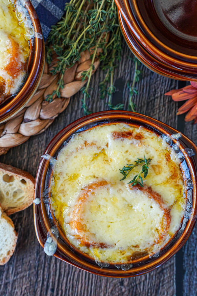 Aerial view of Vegetarian French Onion Soup in a brown bowl with two thyme sprigs on top.