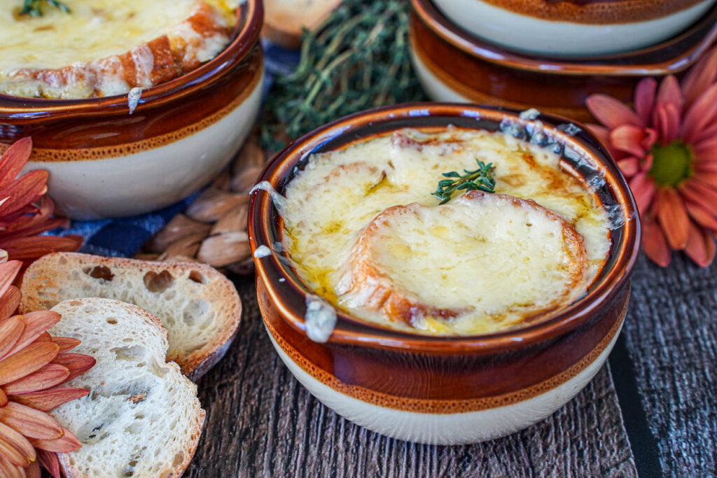 Vegetarian French Onion Soup in two brown bowls next to baguette slices and orange flowers.