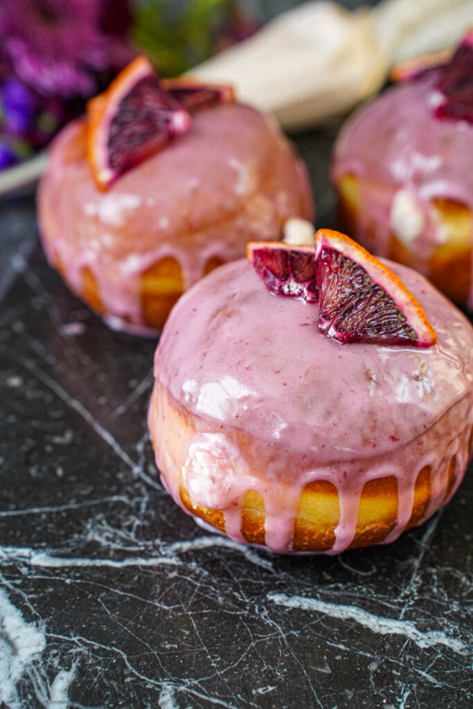 Close up of Blood Orange Cream Cheese Doughnuts topped with blood orange slices and a blood orange glaze.