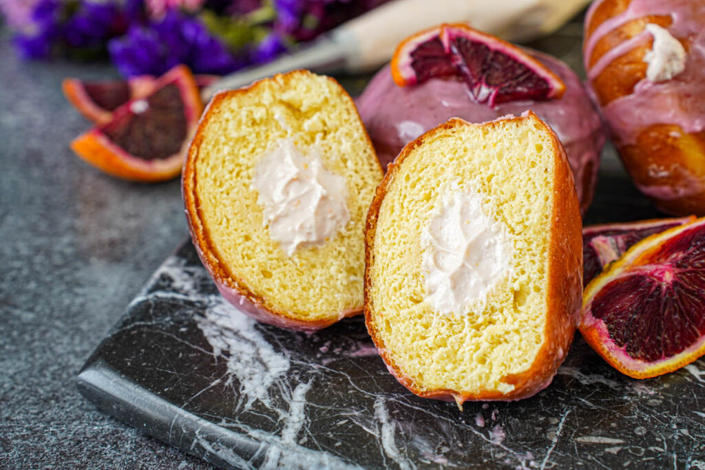 Blood Orange Cream Cheese Doughnuts on a marble board with one cut in half to show cream cheese filling.