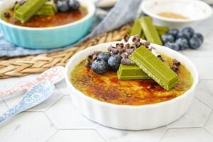 Green Tea Crème Brûlée in two ramekins with whipped cream, matcha Kit Kats and blueberries.