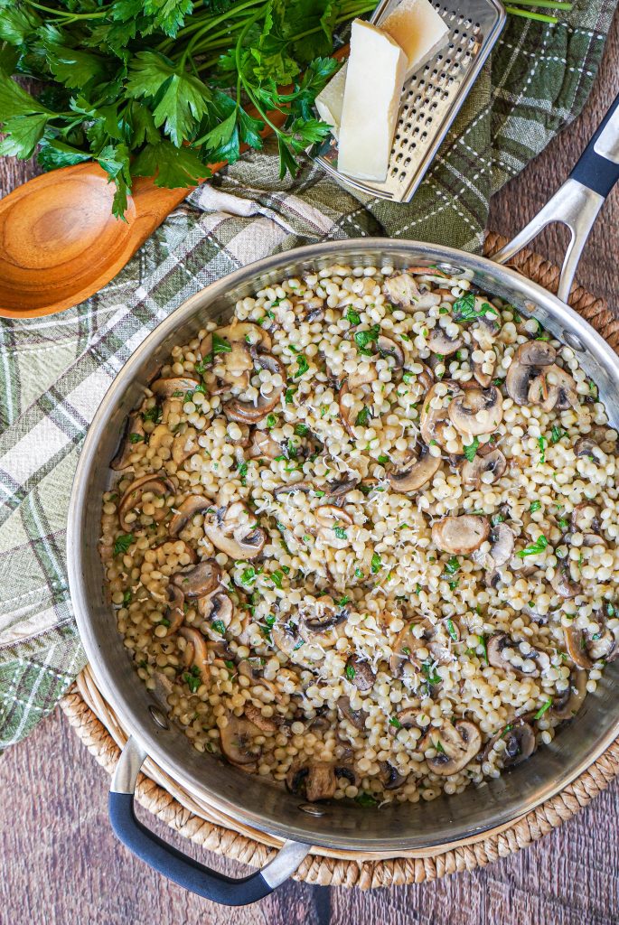 Pearl Couscous with Mushrooms Aerial view of Pearl Couscous with Mushrooms in a pan next to a spoon and parsley.