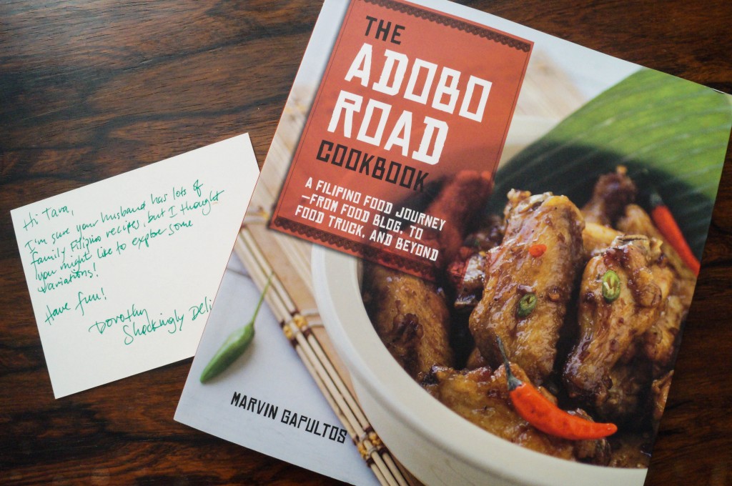 Cookbook resting on a table next to a notecard- The Adobo Road Cookbook by Marvin Gapultos. 