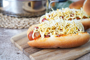 Cachorro Quente (Brazilian Hot Dog) on a wooden board with shoestring potatoes and Parmesan cheese.