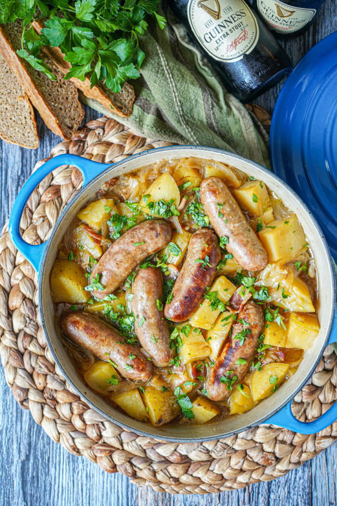 Aerial view of Dublin Coddle (Irish Sausage and Potato Stew) in a blue pot next to bread and parsley.