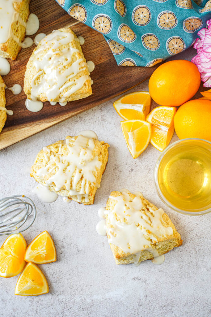Aerial view of Meyer Lemon Scones next to a whisk, Meyer lemons, a lemon towel, and a glass of tea.