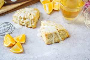 Two Meyer Lemon Scones next to Meyer lemon wedges, a whisk, and a glass of tea.