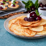 Plättar (Swedish Mini Pancakes) piled on a plate with lingonberry jam and whipped cream.