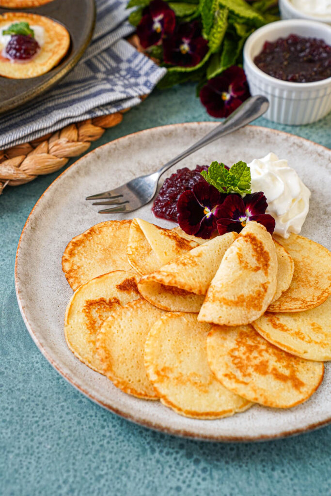 Plättar (Swedish Mini Pancakes) on a plate with three on top folded in half.