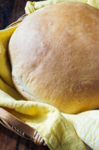 A loaf of Yemarina Yewotet Dabo (Ethiopian Honey Milk Bread) in a basket with a yellow towel.
