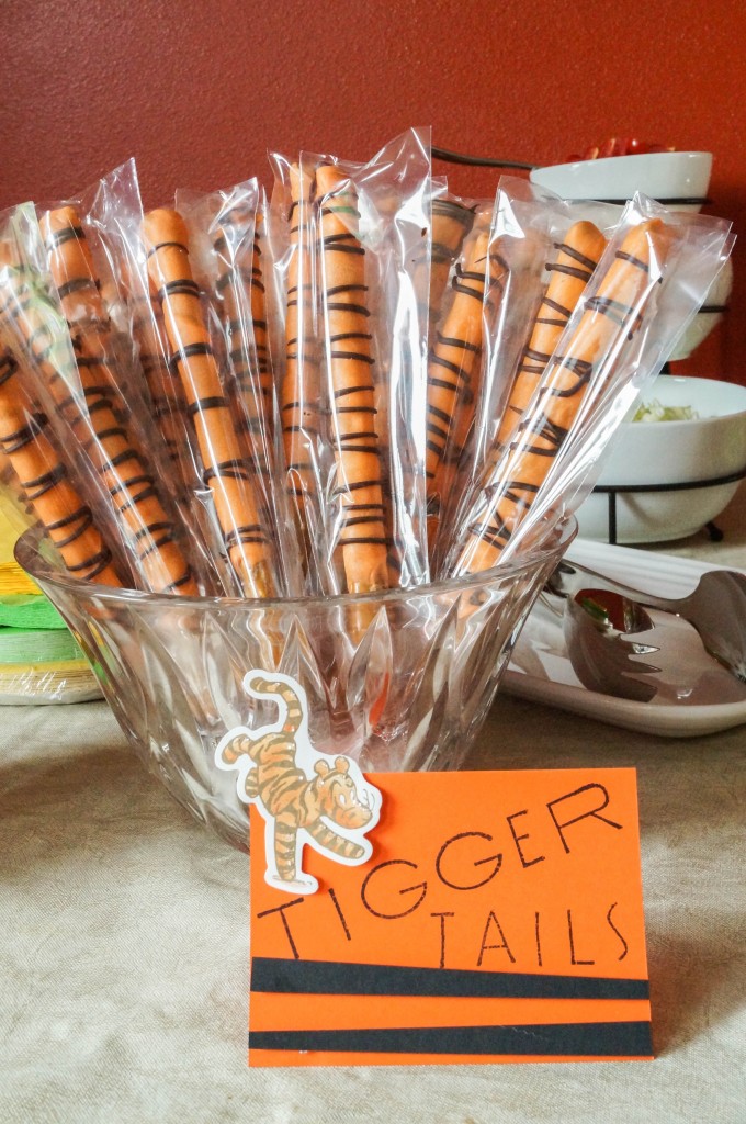 Tigger Tails (orange covered pretzel rods) wrapped in plastic and assembled in a glass bowl.