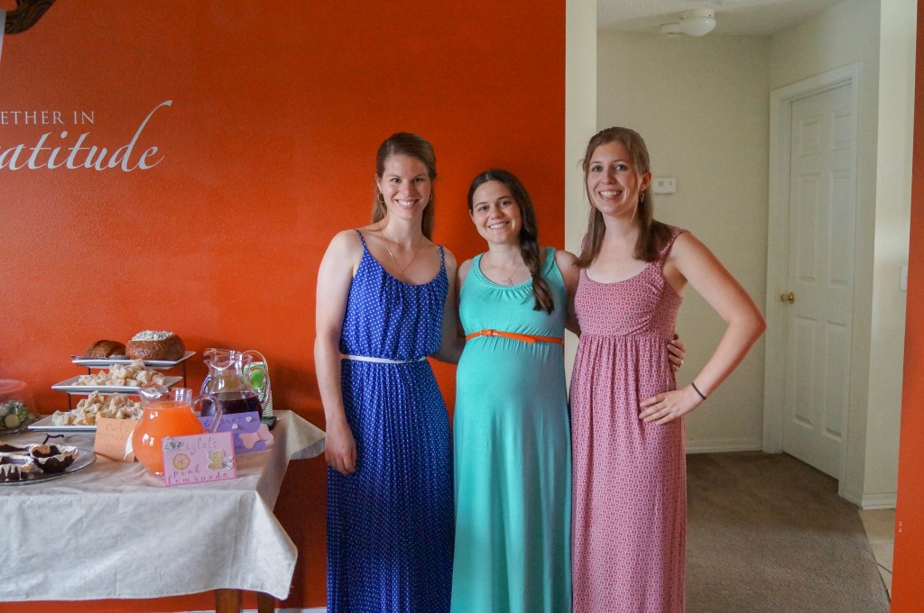 Three women standing together next to food table.