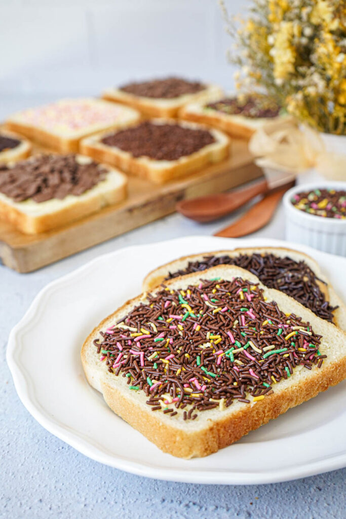 Side view of Broodje Hagelslag (Dutch Bread with Sprinkles) on a white plate with more in the background.