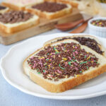 Broodje Hagelslag (Dutch Bread with Sprinkles) on a white plate with more on a wooden board.