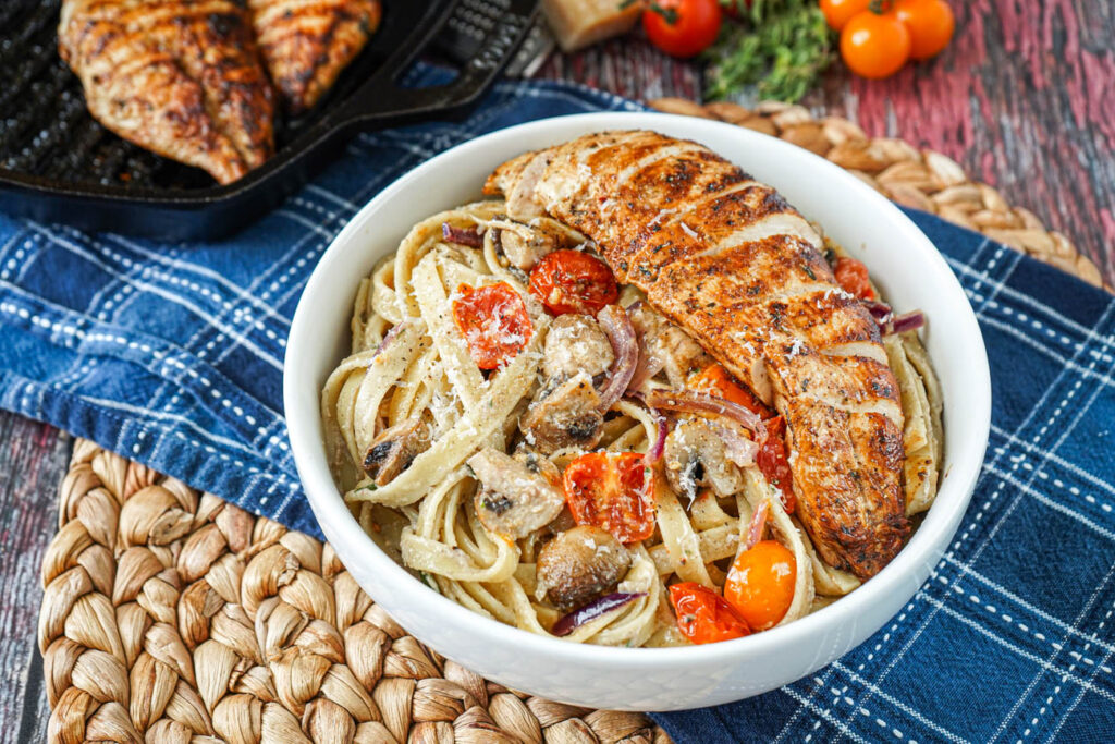 Fettuccine with Mushroom Cream Sauce in a white bowl with sliced chicken.
