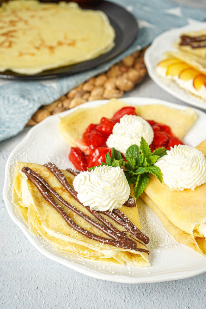 Close up of Sweet Crepe Trio with whipped cream and fresh mint springs on a white plate.