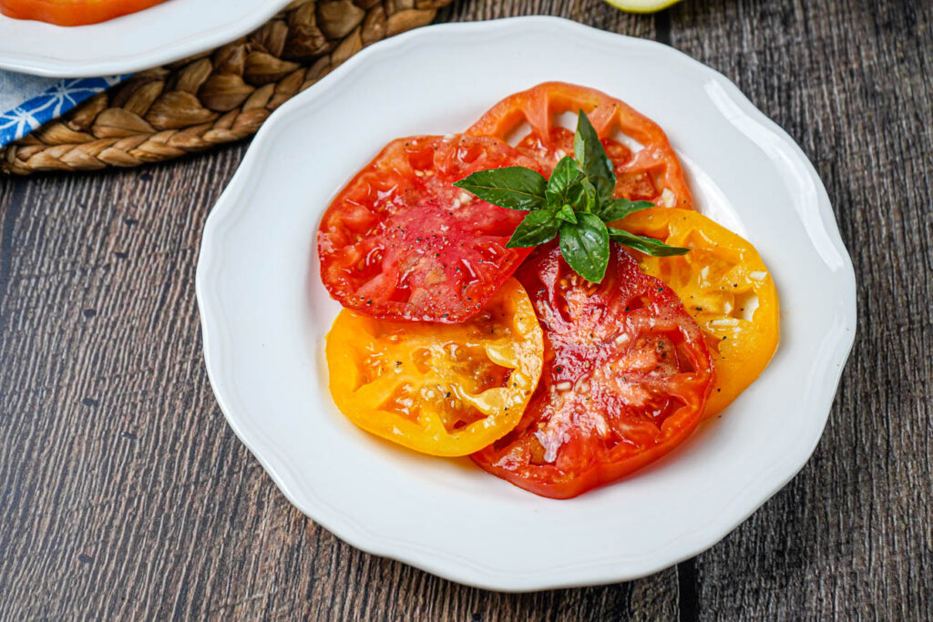 Tomato Salad with Lemon Dijon Dressing on a white plate with fresh basil leaves.