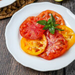 Tomato Salad with Lemon Dijon Dressing on a white plate with fresh basil leaves on top.