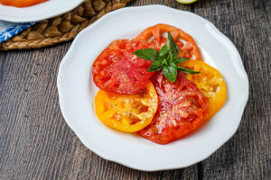 Tomato Salad with Lemon Dijon Dressing on a white plate with fresh basil leaves on top.
