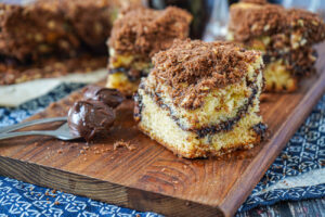 Three slices of Nutella Coffee Cake on a wooden board next to two spoons with Nutella.
