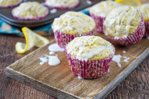 Lemon Poppy Seed Muffins on a wooden board and in muffin tins with a drizzle of lemon glaze.