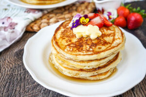 Vanilla Bean Buttermilk Pancakes in a stack and topped with butter, edible flowers, and strawberries.