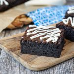 Three Dark Chocolate Brownies with a White Chocolate Drizzle on a wooden board.