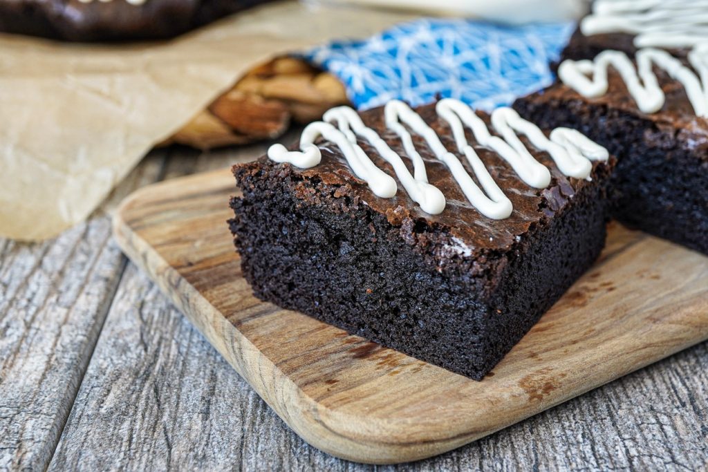 Close up of Dark Chocolate Brownies with white chocolate drizzle on a wooden board.