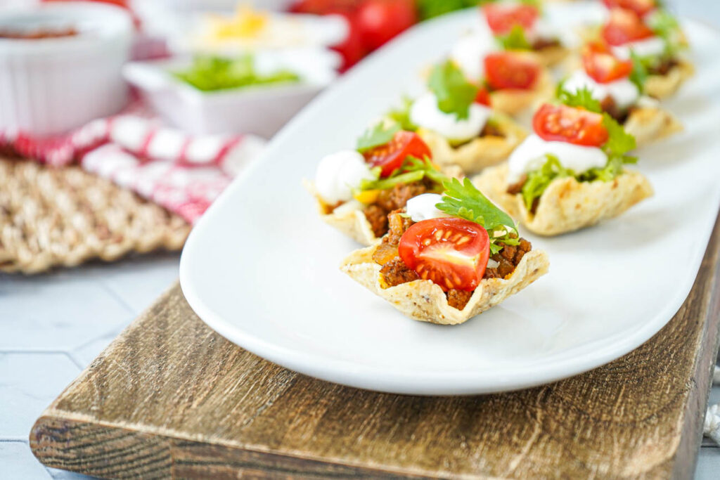 Mini Taco Bites on a white platter topped with cherry tomatoes, cilantro, and sour cream.