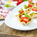 Mini Taco Bites on a white platter with cherry tomatoes, cilantro, and sour cream.