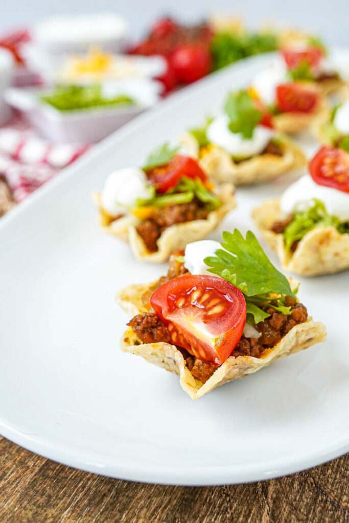 Close up of Mini Taco Bites with a cherry tomato quarter, cilantro, and sour cream.