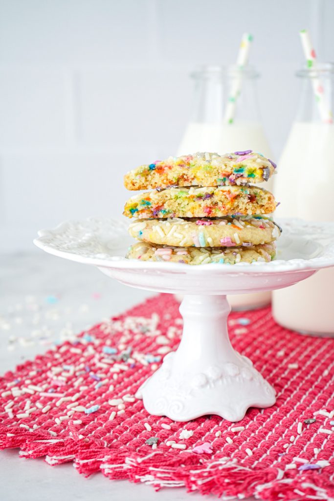 A stack of four Sprinkle Sugar Cookies with the top two cut in half to show sprinkle filling.