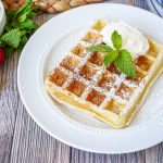 Gaufre de Bruxelles (Brussels Waffle) on a white plate with mint and whipped cream.