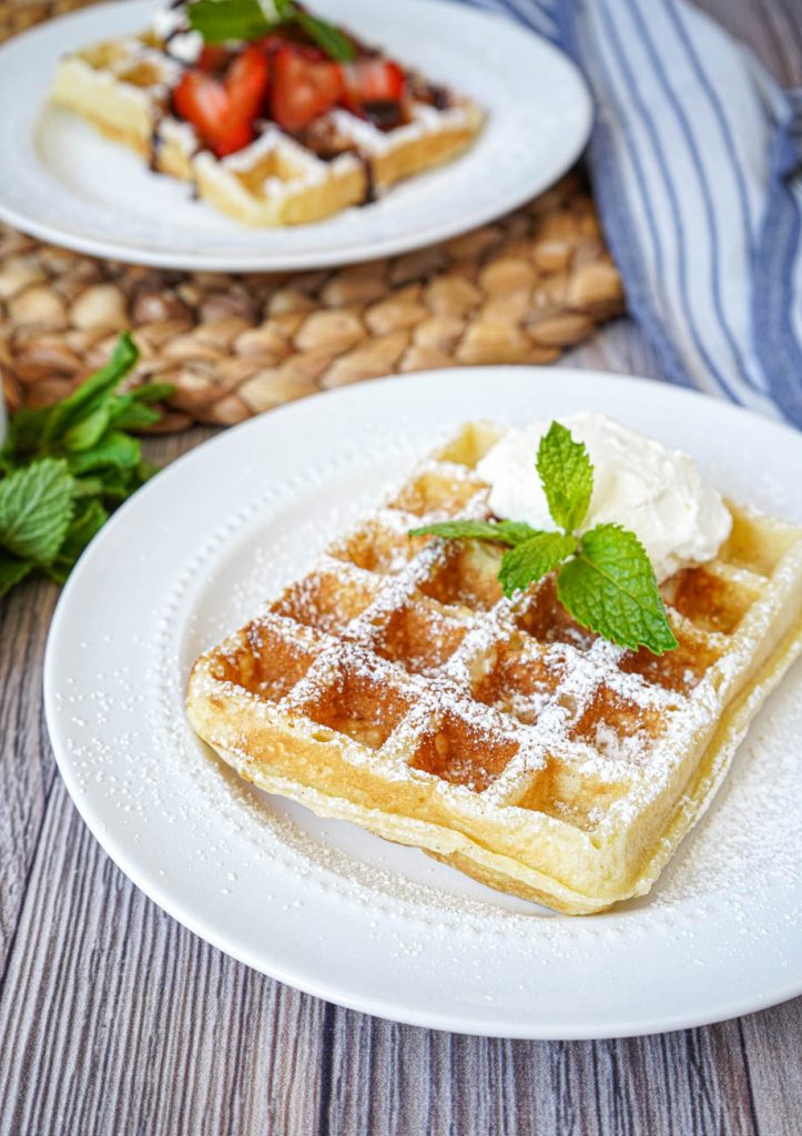 Close up of Gaufre de Bruxelles (Brussels Waffle) on two white plates with mint.