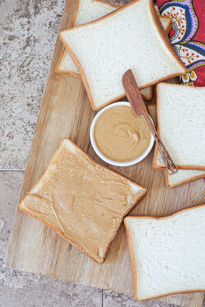 Spreading peanut butter over a slice of bread next to 5 more slices of bread.